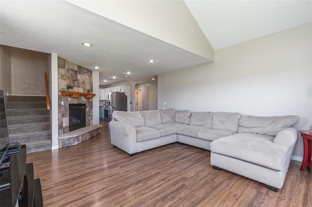 living room featuring a textured ceiling, lofted ceiling, a stone fireplace, and wood-type flooring