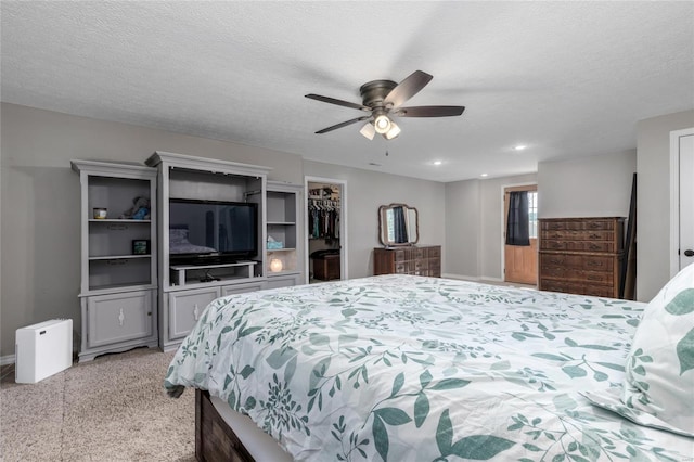 carpeted bedroom with a walk in closet, ceiling fan, and a textured ceiling