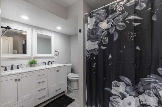 bathroom with double vanity, a textured ceiling, and toilet