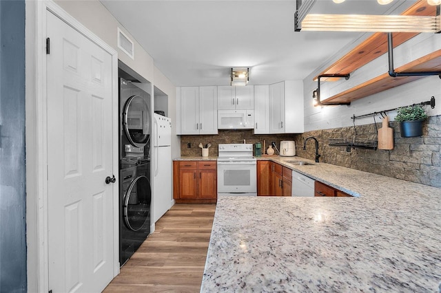 kitchen with white appliances, stacked washer and dryer, sink, decorative backsplash, and light wood-type flooring