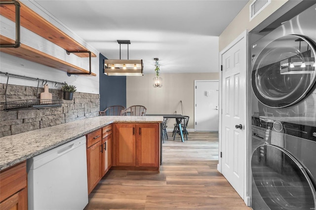 kitchen featuring stacked washer and clothes dryer, decorative light fixtures, wood-type flooring, white dishwasher, and light stone countertops