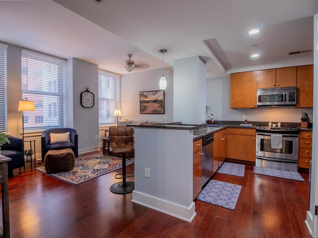 kitchen featuring ceiling fan, dark hardwood / wood-style floors, kitchen peninsula, appliances with stainless steel finishes, and a breakfast bar area