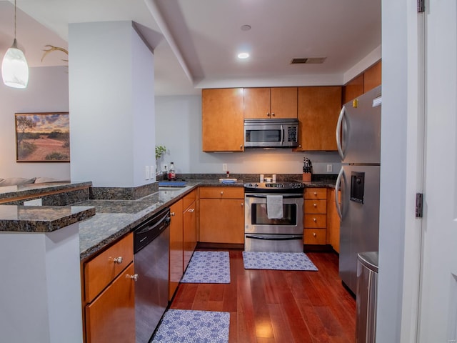 kitchen with dark hardwood / wood-style flooring, kitchen peninsula, appliances with stainless steel finishes, and hanging light fixtures