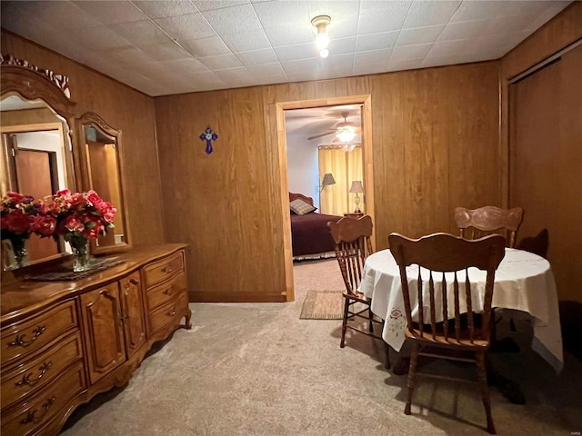 dining room featuring light colored carpet, wooden walls, and ceiling fan