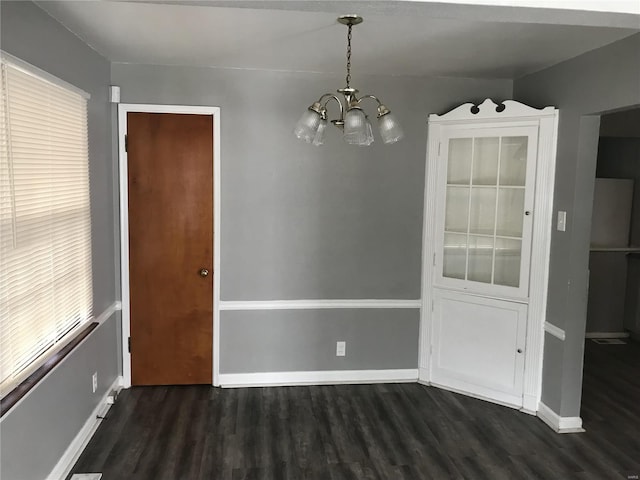 unfurnished dining area with dark wood finished floors, baseboards, and an inviting chandelier