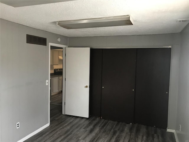 unfurnished bedroom featuring a textured ceiling, dark hardwood / wood-style floors, and a closet