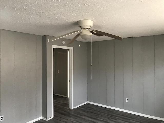 unfurnished room with a textured ceiling, dark hardwood / wood-style floors, wooden walls, and ceiling fan