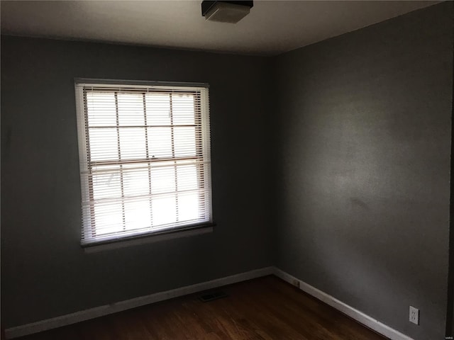 empty room with baseboards, visible vents, dark wood-style floors, and plenty of natural light