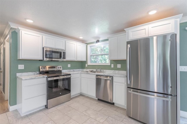 kitchen featuring appliances with stainless steel finishes, white cabinetry, light stone countertops, a textured ceiling, and crown molding