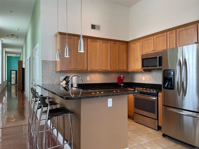 kitchen featuring stainless steel appliances, decorative light fixtures, light wood-type flooring, dark stone countertops, and a towering ceiling