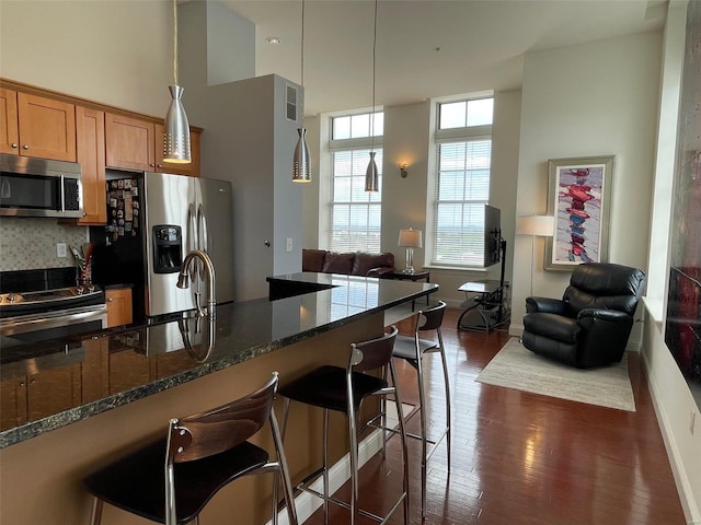 kitchen featuring decorative backsplash, dark hardwood / wood-style floors, a high ceiling, dark stone countertops, and stainless steel appliances