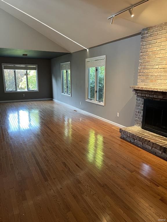 unfurnished living room with a wealth of natural light, wood-type flooring, vaulted ceiling, and rail lighting