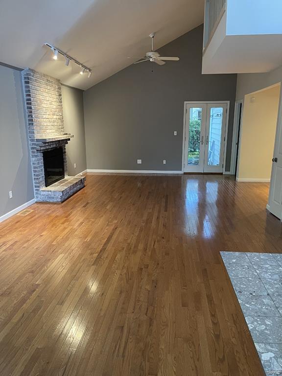 unfurnished living room featuring a stone fireplace, french doors, wood-type flooring, track lighting, and ceiling fan