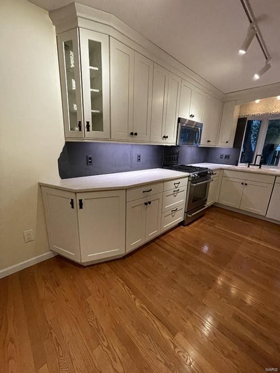 kitchen with light wood-type flooring, white cabinets, rail lighting, and stainless steel appliances