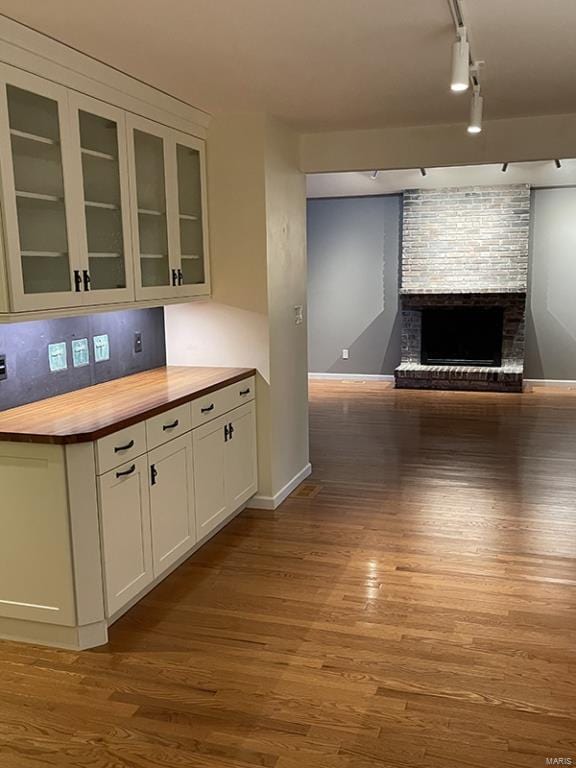 kitchen featuring track lighting, wooden counters, backsplash, a fireplace, and light wood-type flooring