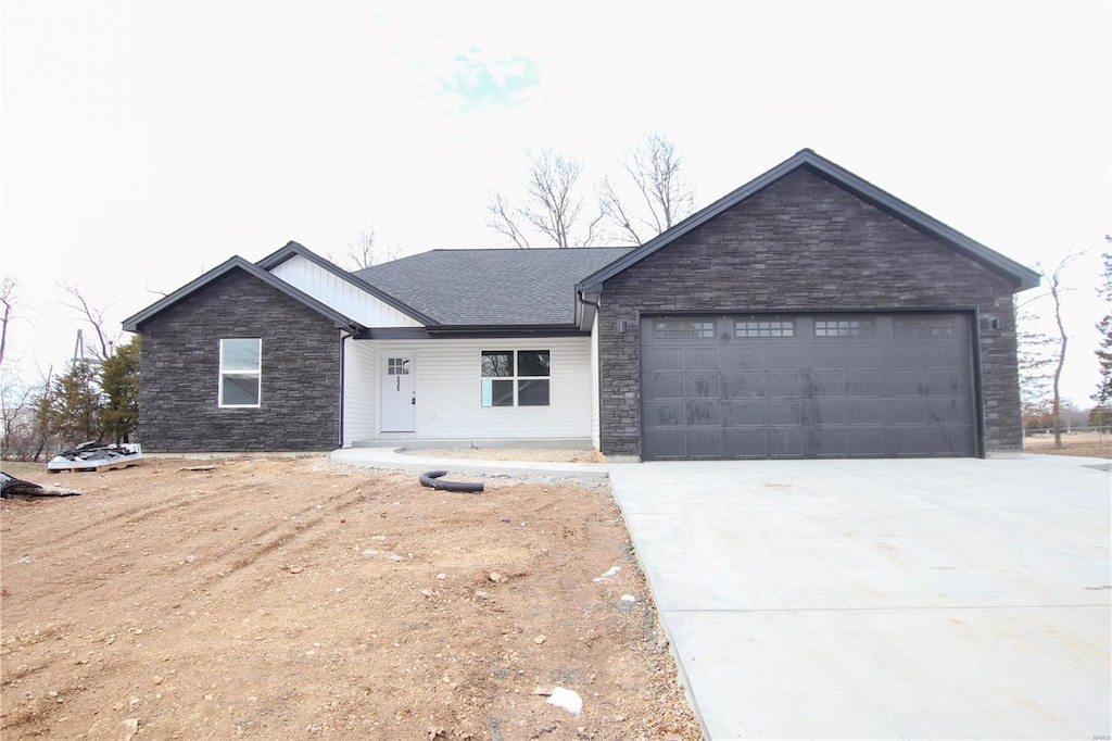 single story home featuring driveway, stone siding, a garage, and roof with shingles