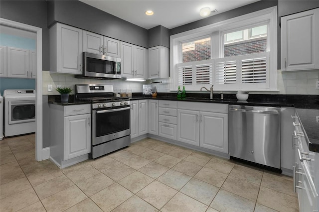 kitchen featuring stainless steel appliances, washer / clothes dryer, dark countertops, and white cabinetry