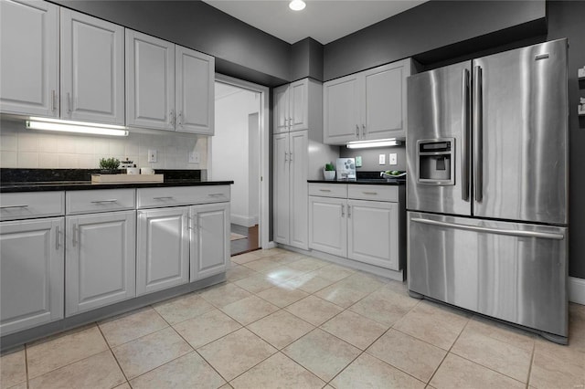 kitchen featuring light tile patterned floors, dark countertops, stainless steel fridge, and white cabinetry