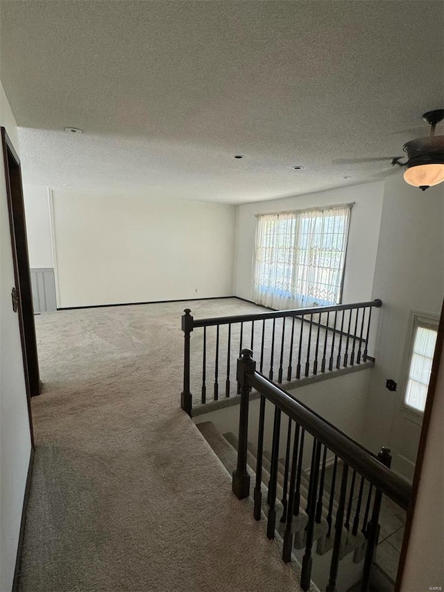 hallway featuring a textured ceiling, carpet, and an upstairs landing