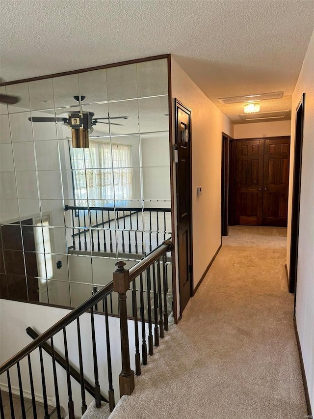 hall featuring a textured ceiling, carpet flooring, and an upstairs landing