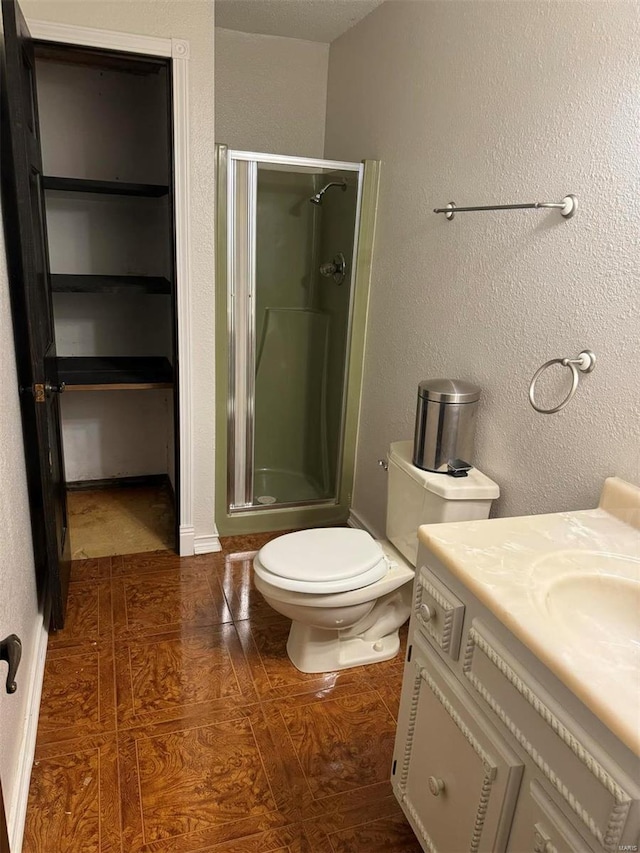 full bath featuring a stall shower, a textured wall, vanity, and toilet