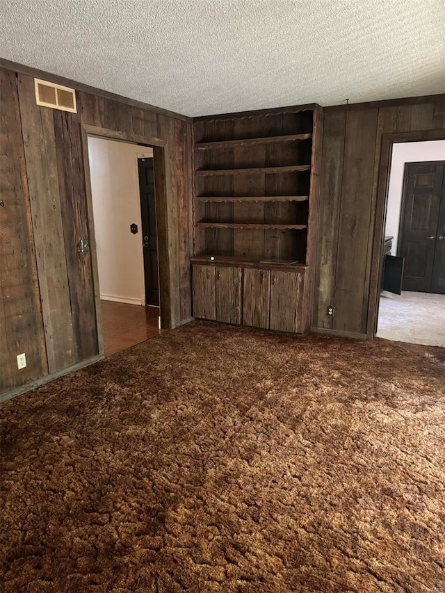 carpeted spare room with a textured ceiling, built in shelves, visible vents, and wooden walls