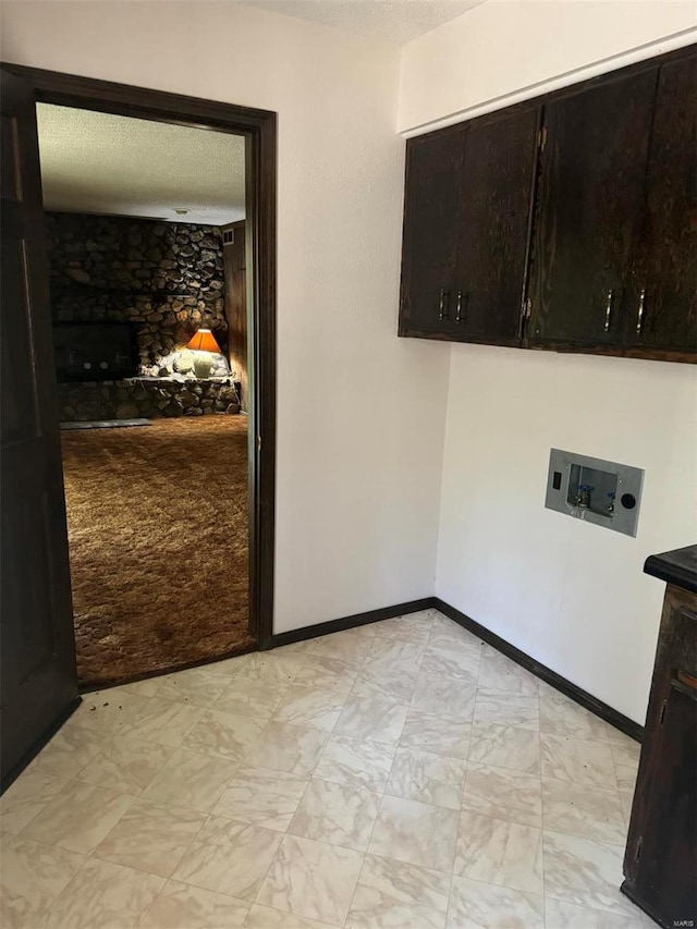 interior space with a textured ceiling, a stone fireplace, and baseboards