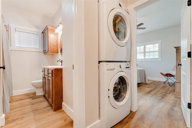 clothes washing area with stacked washing maching and dryer, ceiling fan, sink, and light hardwood / wood-style floors