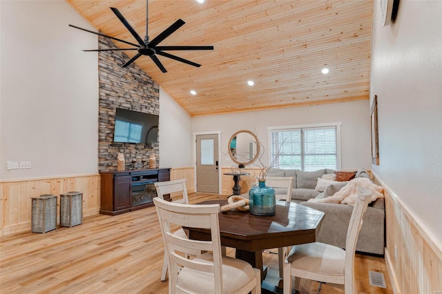 dining area featuring wood walls, wooden ceiling, high vaulted ceiling, ceiling fan, and light wood-type flooring