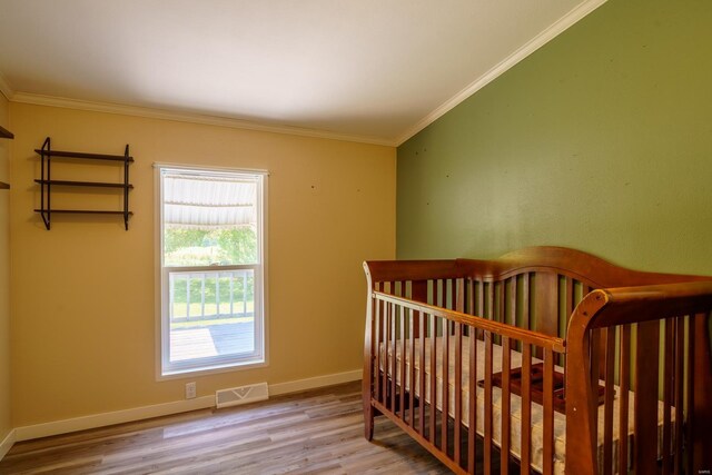 bedroom featuring hardwood / wood-style flooring, a nursery area, and crown molding