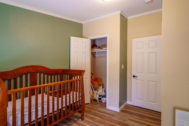 bedroom with a closet, a nursery area, crown molding, and wood-type flooring