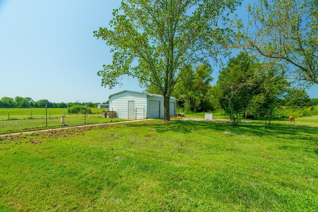 view of yard with a garage, a rural view, an outdoor structure, and fence