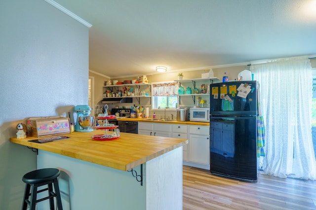 kitchen featuring wooden counters, ornamental molding, white cabinets, a sink, and black appliances