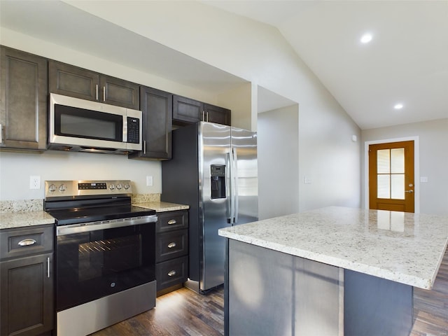 kitchen with dark wood-type flooring, a kitchen island, vaulted ceiling, light stone counters, and stainless steel appliances