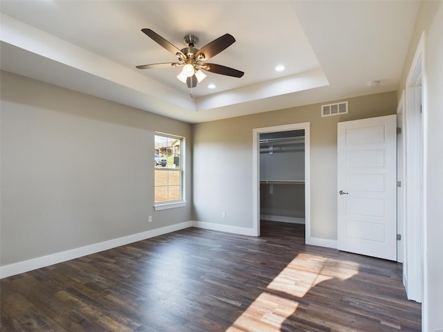 unfurnished bedroom featuring a walk in closet, dark hardwood / wood-style flooring, a tray ceiling, a closet, and ceiling fan