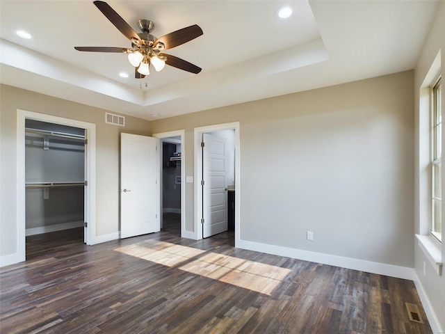 unfurnished bedroom with ceiling fan, a raised ceiling, and dark wood-type flooring