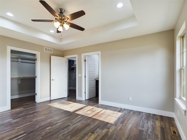 unfurnished bedroom with ceiling fan, a tray ceiling, and dark hardwood / wood-style floors