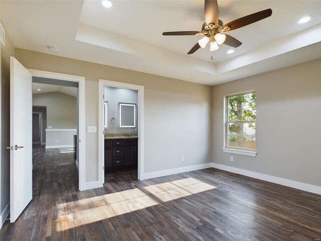 unfurnished bedroom with ceiling fan, a raised ceiling, dark hardwood / wood-style flooring, and ensuite bath