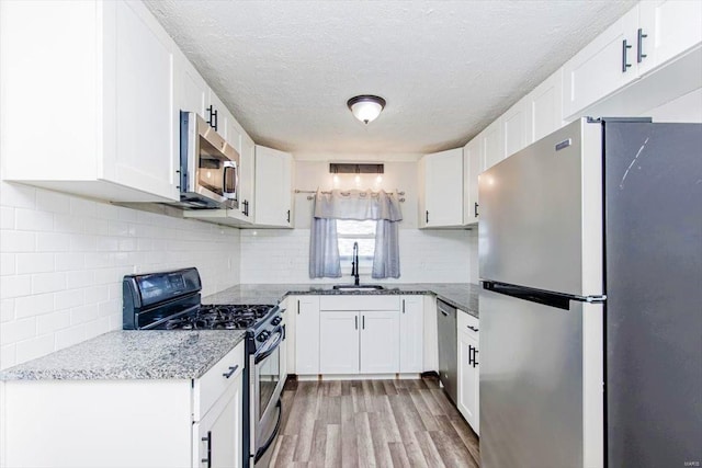 kitchen featuring backsplash, stainless steel appliances, sink, light wood-type flooring, and white cabinets