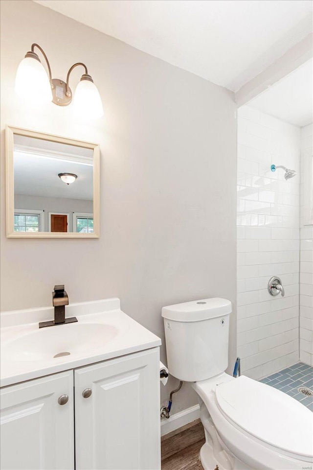 bathroom with toilet, vanity, tiled shower, and wood-type flooring