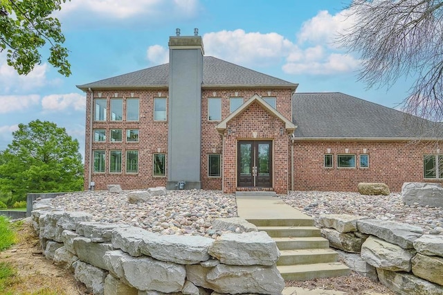 rear view of property with french doors, a chimney, a shingled roof, and brick siding