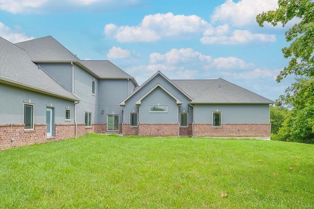 rear view of house featuring brick siding, stucco siding, and a yard
