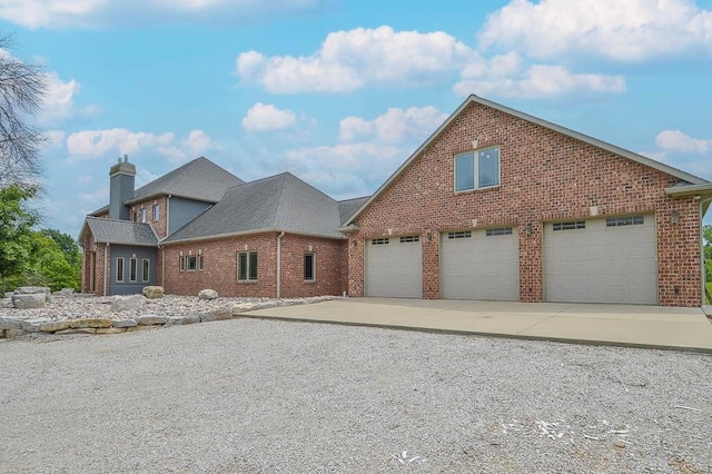view of front facade featuring concrete driveway, brick siding, a chimney, and a garage