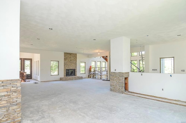 unfurnished living room featuring concrete floors, a stone fireplace, and a wealth of natural light