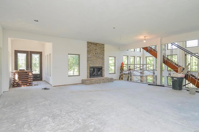 unfurnished living room featuring a stone fireplace, concrete flooring, and french doors