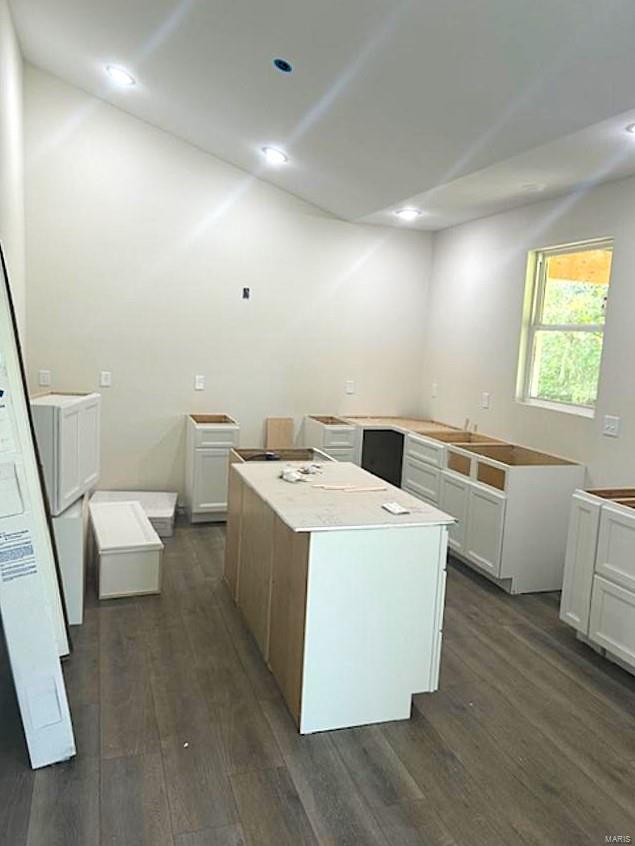 kitchen with dark hardwood / wood-style floors, lofted ceiling, a kitchen island, and white cabinets