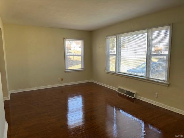 empty room featuring dark wood-style floors, visible vents, and baseboards