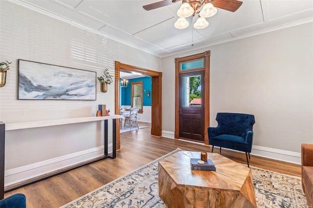 living area featuring a ceiling fan, baseboards, ornamental molding, and wood finished floors