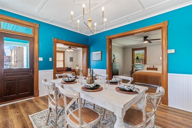 dining room with ceiling fan with notable chandelier, ornamental molding, wood finished floors, and wainscoting