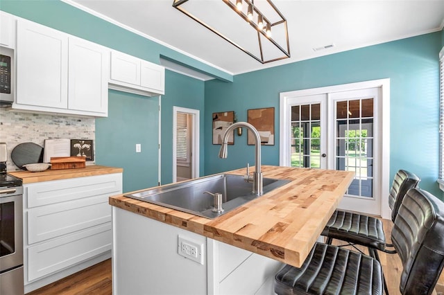 kitchen featuring tasteful backsplash, butcher block counters, appliances with stainless steel finishes, french doors, and a sink